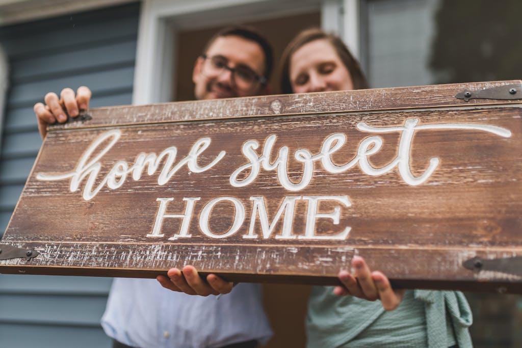 A joyful couple holding a 'home sweet home' sign in front of their new house.